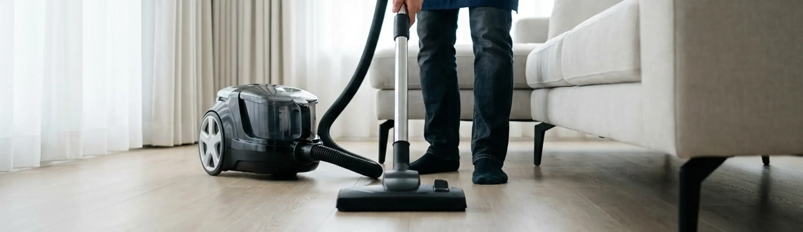 Professional house cleaner vacuuming a living room floor with a canister vacuum cleaner, Long Beach, CA.