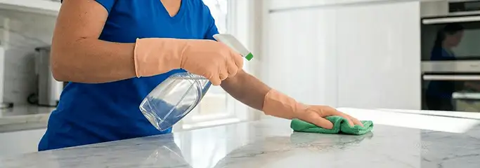 Maid service worker spraying and wiping a kitchen countertop with a microfiber cloth for sanitizing, Long Beach, CA.
