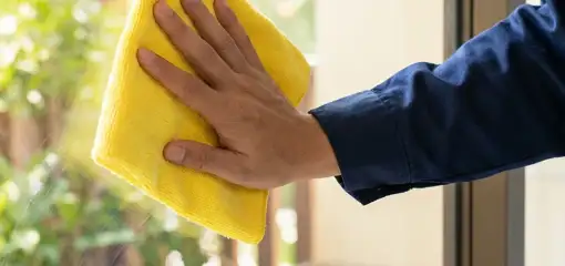 House cleaner wiping a glass window with a yellow microfiber cloth for streak-free cleaning, Long Beach, CA.